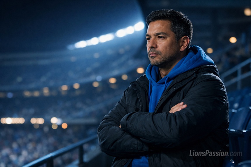 Detroit Lions fan in upper deck at night wearing blue hoodie and winter jacket, arms folded, serious analytical expression