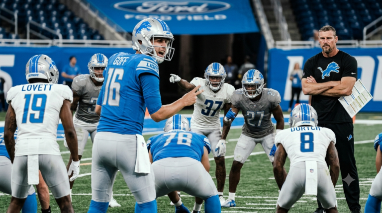Detroit Lions players practice a situational football drill during training camp while Dan Campbell watches.